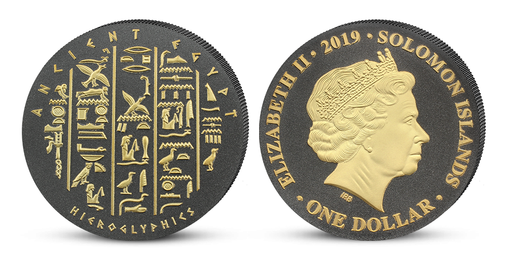 Minca s egyptskými hieroglyfmi v parciálnom zušľachtení rýdzim zlatom a čiernym niklom Minca s egyptskými hieroglyfmi v parciálnom zušľachtení rýdzim zlatom a čiernym niklom